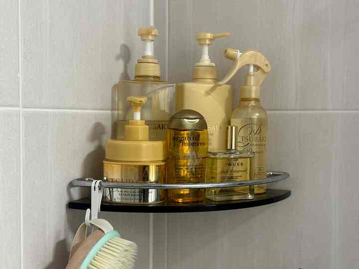 淡いグレーのタイル壁に設置された黒いコーナー棚にゴールド調のバス用品が並ぶバスルーム