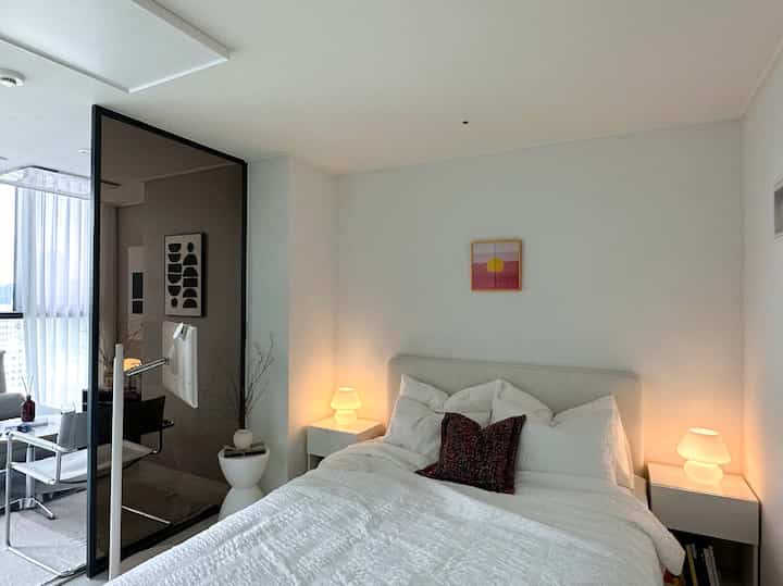 白色トーンの寝室、ベッドとナイトテーブル上のテーブルランプが配置されたシンプルでモダンなインテリア