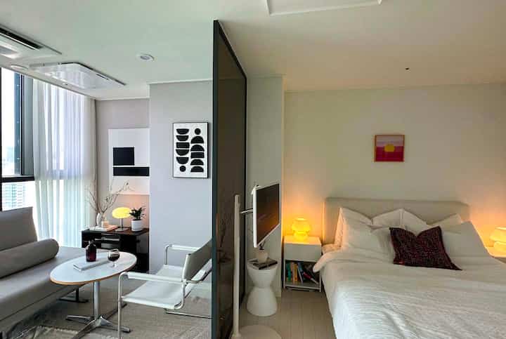 白とベージュのトーンのワンルーム空間、スクリーンで区切られた寝室とリビングが配置されたシンプルモダンなインテリア