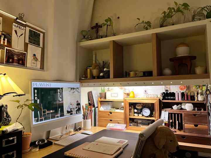 白い壁と木目調家具が調和したモダンでナチュラルなホームオフィス空間、机とパソコン、多様なオブジェや植物が置かれた落ち着いた作業空間