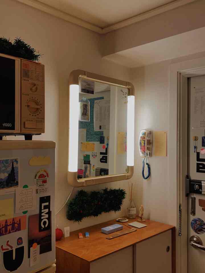 白い壁と木目調の収納がある玄関、両側に照明が付いたヴィンテージ風の鏡が印象的な明るい空間