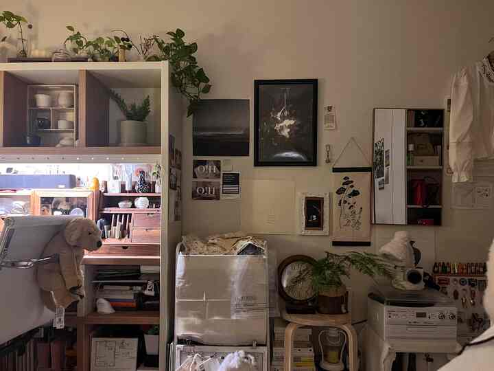 ホワイトとブラウンのトーンが調和する小さな部屋、植物と犬のぬいぐるみ、壁飾りが印象的な雰囲気のあるインテリア