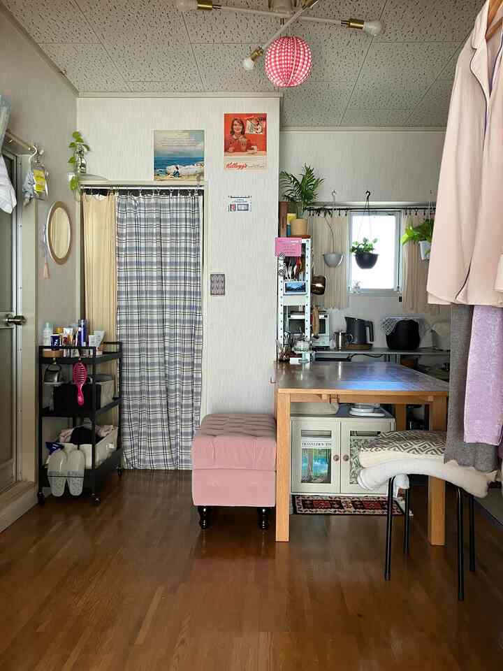 白と木目調のコンパクトなワンルーム、ピンクのスツールとキッチンが調和した雰囲気のあるインテリア