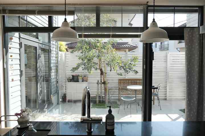 白とグレーのトーンのモダンなキッチン、透明なガラス越しに中庭とベランダが見える開放的な空間