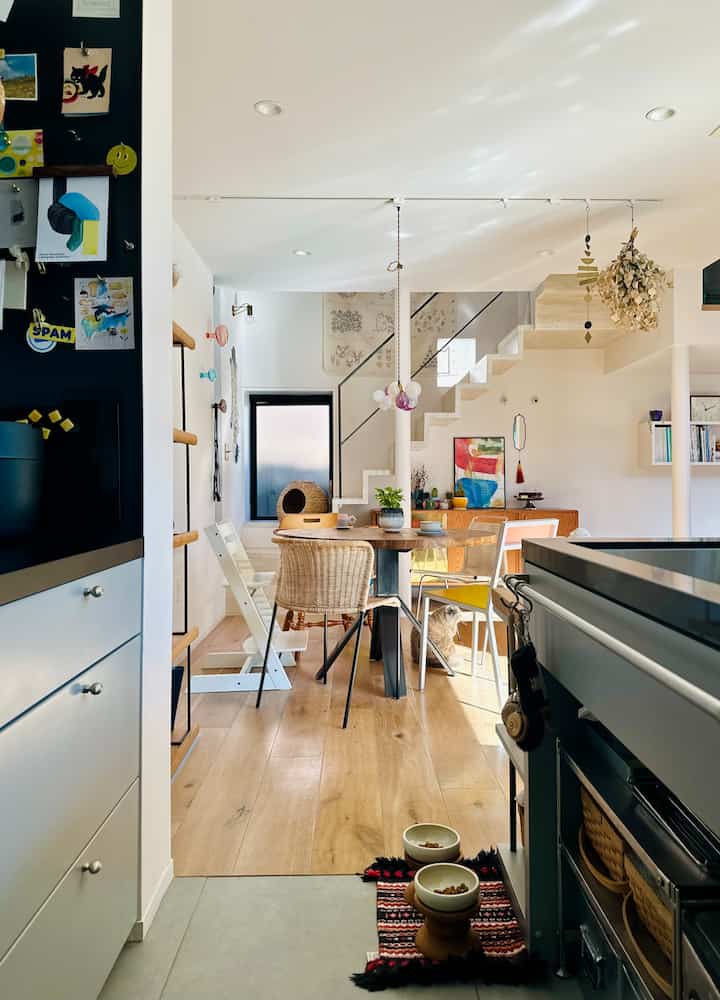 ナチュラルカラーとホワイトの色調のキッチンとダイニング、丸いダイニングテーブルと様々な素材の椅子が配置された雰囲気のある空間