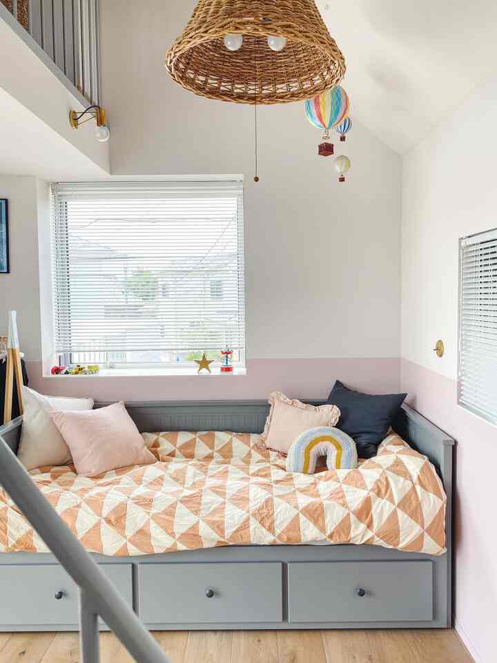 ピンクとホワイトの壁分けとグレーのデイベッド、クッションが配置された明るくすっきりとした子供部屋のインテリア