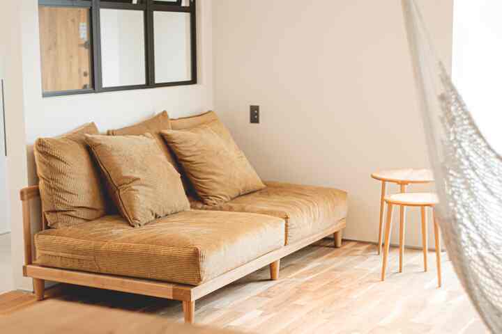 ナチュラルカラーのリビング、広いベージュのソファと丸い木製サイドテーブルが配置された落ち着いた雰囲気の空間