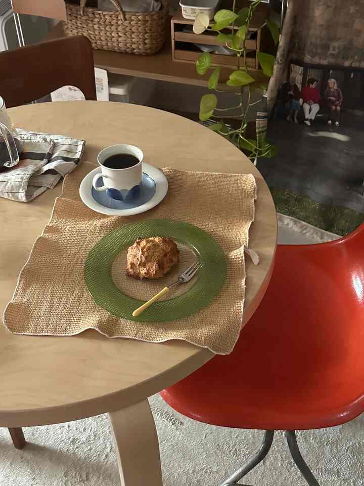ナチュラルな木目調のダイニングルーム、中央にコーヒーカップとペストリーが置かれた木製テーブルがある温かみのある空間