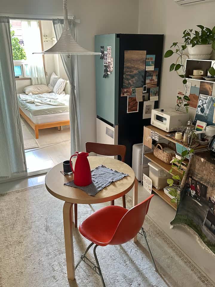 ナチュラルな木目調とレッドのアクセントがあるコンパクトなワンルームのキッチンと寝室のインテリア