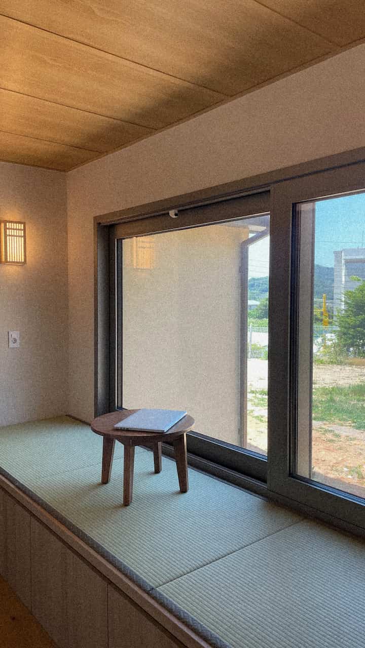 ナチュラルな色調の寝室コーナー、大きな窓と低い収納キャビネットに畳が敷かれた雰囲気のあるインテリア