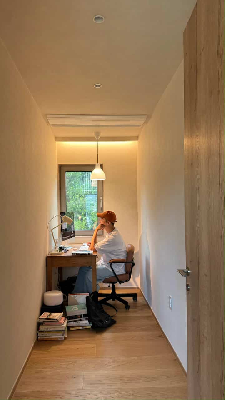 ナチュラルな木目調と白い壁の狭い書斎、窓際に置かれたデスクと椅子が落ち着いたホームオフィス空間を演出