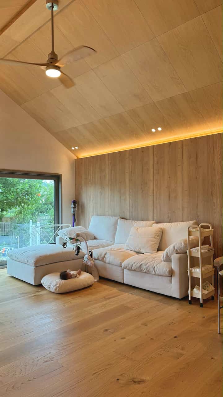 温かみのあるナチュラルカラーと木目調のリビング、ソファと赤ちゃんスペースが配置された雰囲気のある空間