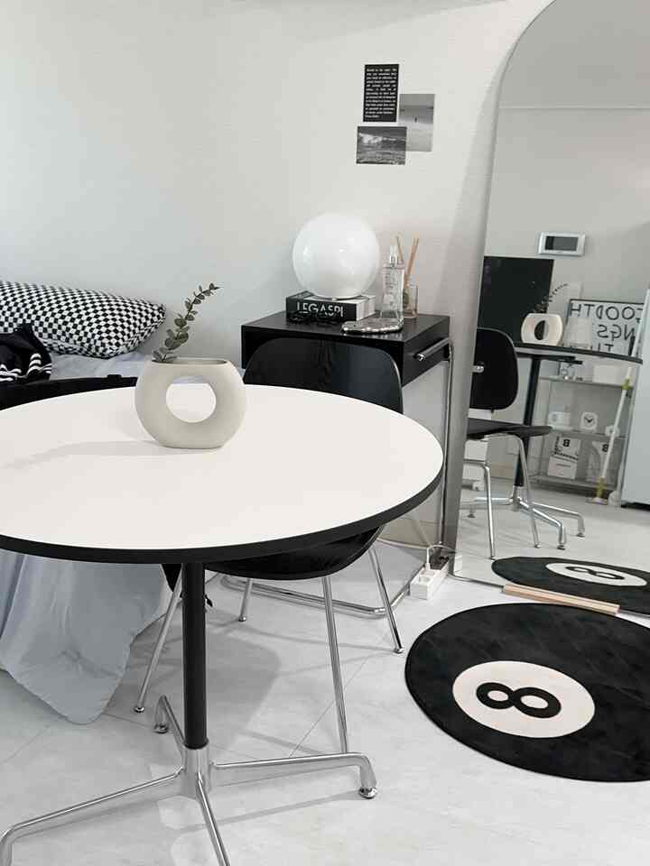 白と黒の色調のリビングルーム、丸いダイニングテーブル、黒い椅子、大きなアーチ型の鏡、丸いラグが配されたモダンなインテリア