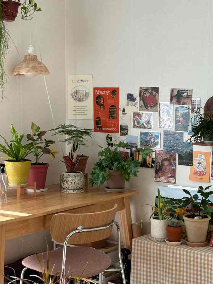 ナチュラルな色調の小さな作業空間、木製のデスクと多様な植物が配置された雰囲気あるインテリア