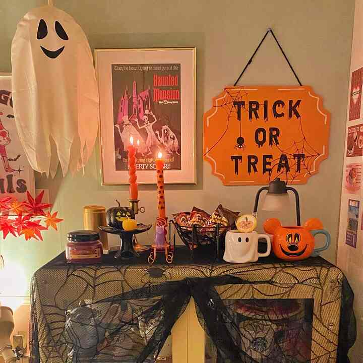黄色いキャビネットの上にハロウィンの飾りと黒いクモの巣模様のテーブルクロスが配置された雰囲気のある空間