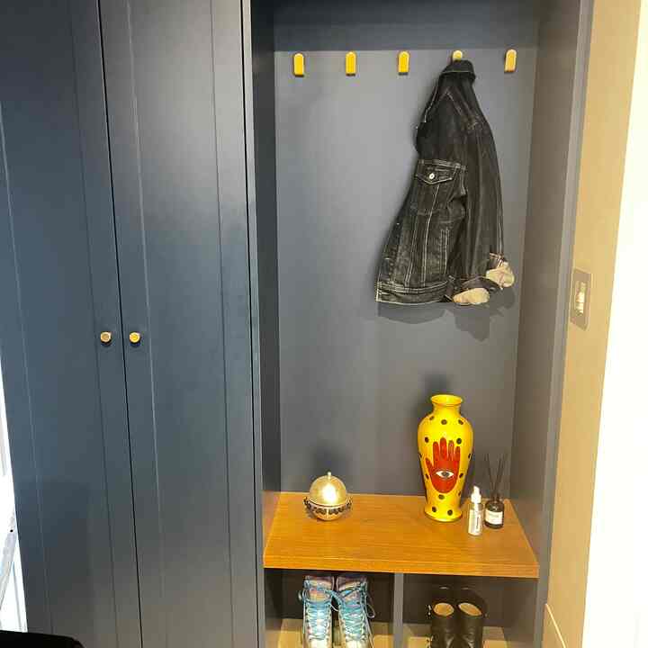 ネイビーブルーの壁と木目調のベンチがあるコンパクトな玄関、黄色いコートハンガーと花瓶を配した印象的な空間