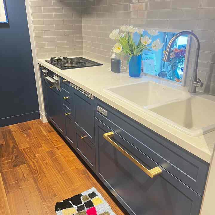 白い大理石のカウンタートップとネイビーのキャビネットが調和したモダンなキッチン、ダブルシンクとゴールドの取っ手が印象的な空間
