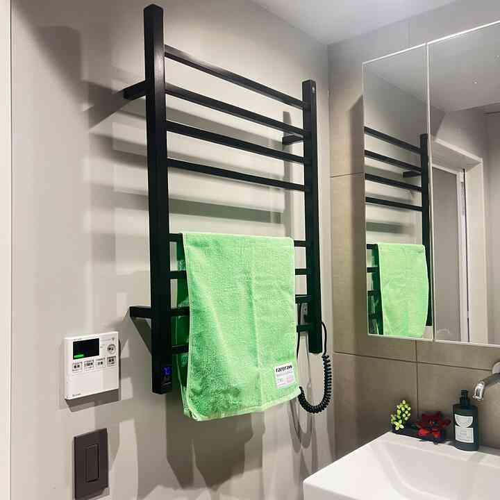 白い壁と洗面台のあるバスルームの壁にブラックのタオル掛けが取り付けられ、明るい緑のタオルが掛けられたシンプルな空間