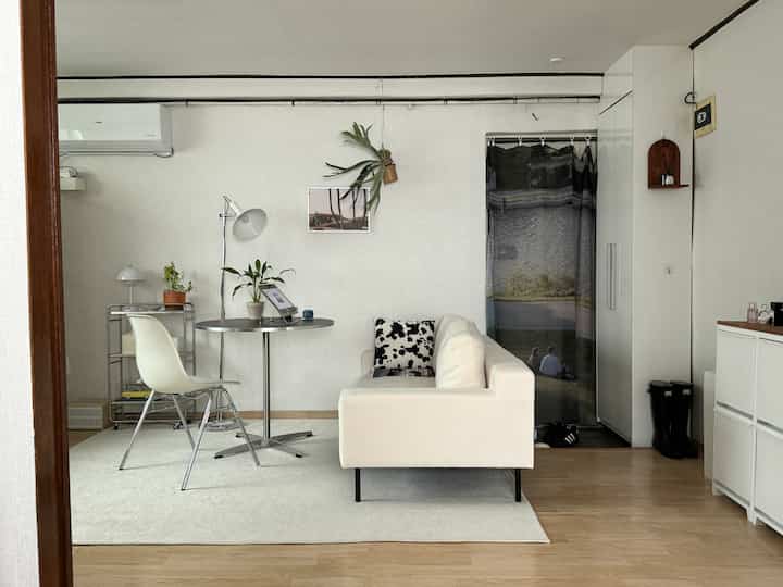 白とグレーの色調のリビング兼キッチン、ソファと円形テーブルが配置された清潔感のあるナチュラルな空間