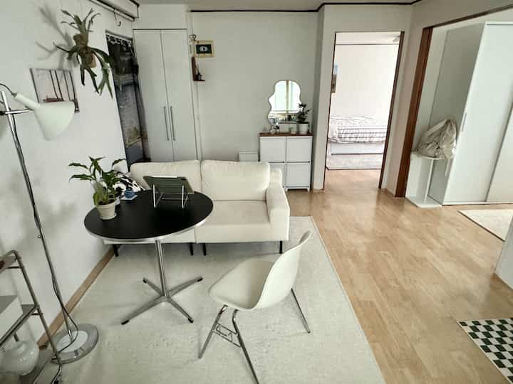 白と木目調の調和が美しいワンルームリビング、ミニマルなソファと円形テーブルが配置された清潔感のあるインテリア