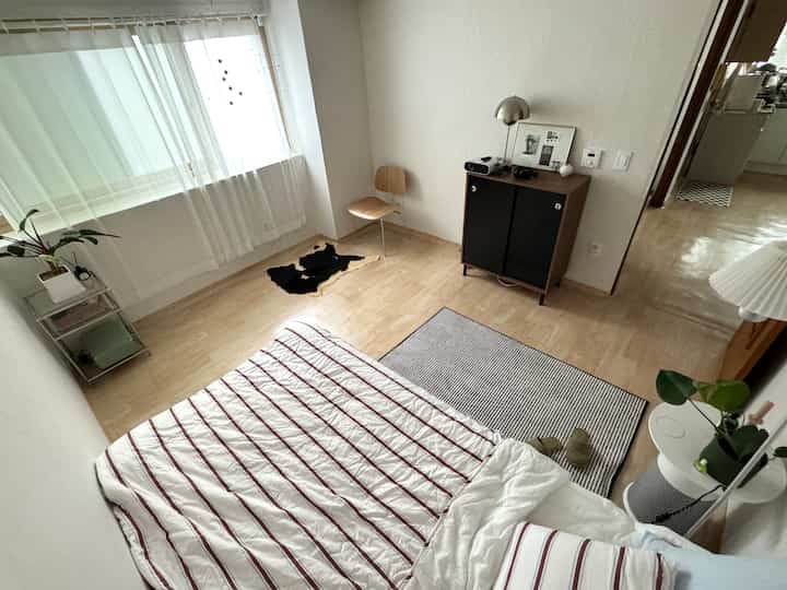 白とナチュラルウッドのトーンが調和した寝室、ベッドとキャビネットがミニマルに配置され、すっきりとした印象的な空間。