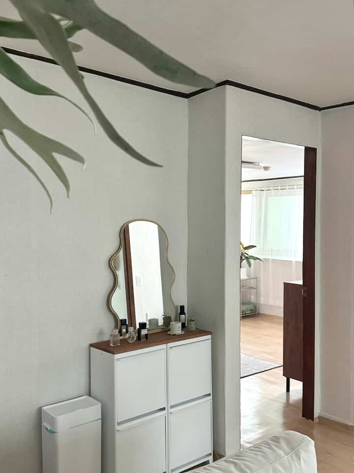 白と木目調のリビング、分別ゴミ箱と独特な形の鏡が置かれたシンプルな収納家具のある空間