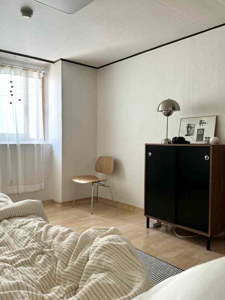 ナチュラルカラーと木目調の寝室、ストライプの寝具とシンプルなキャビネットが配置された落ち着いた空間