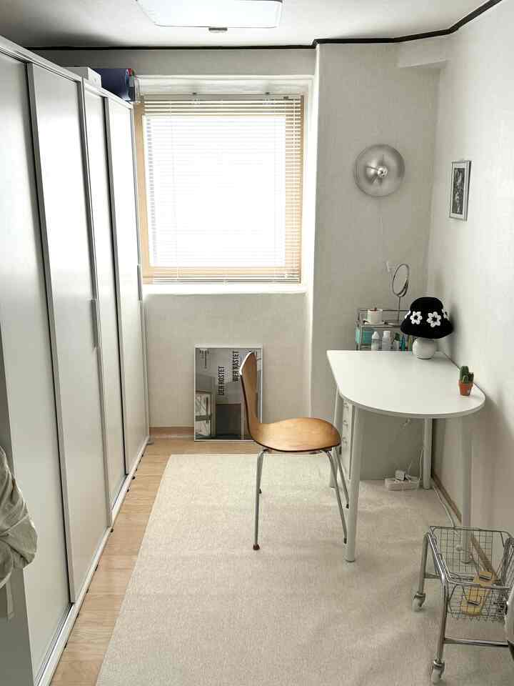 白い壁と家具、木目の椅子とスライド式クローゼットが配置されたコンパクトなホームオフィスの空間