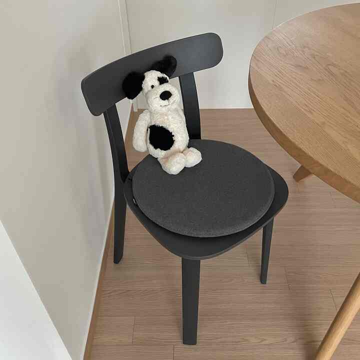 ナチュラルな木目調のダイニング空間、黒い椅子の上に犬のぬいぐるみが置かれている印象的なインテリア