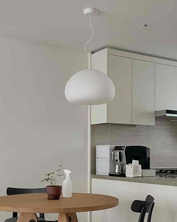 ホワイトと木目調のモダンなキッチン・ダイニング空間、中央にムートのペンダントライトと丸いダイニングテーブルが配置されている