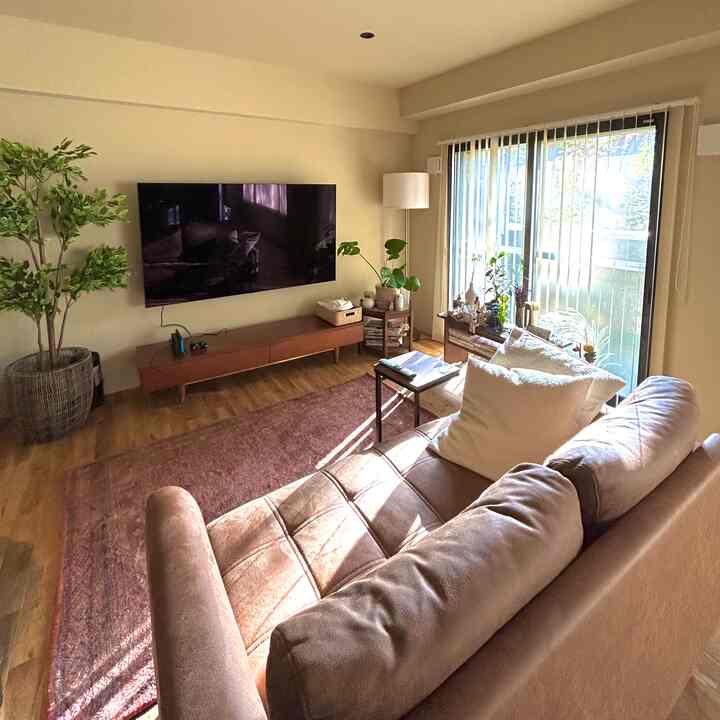 ベージュとブラウンを基調としたリビング、広いソファとテレビ台、緑の植物と赤いラグが配置された雰囲気のあるインテリア