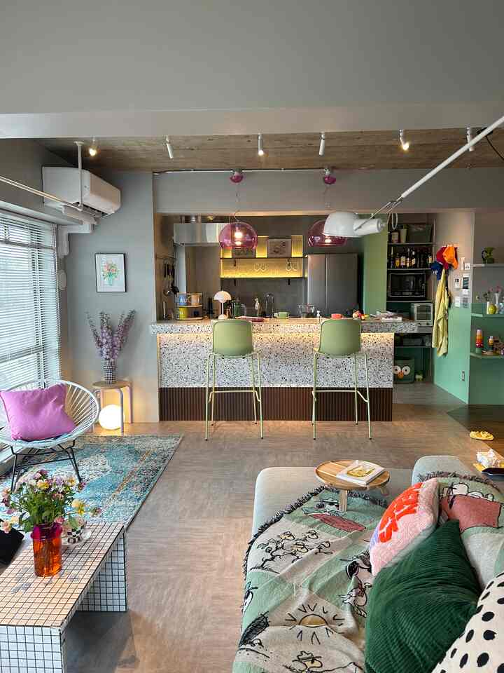 ナチュラルトーンのオープンキッチンとリビング、ライムグリーンのカウンタースツールと紫のペンダントライトが特徴の20畳LDKの印象的なインテリア