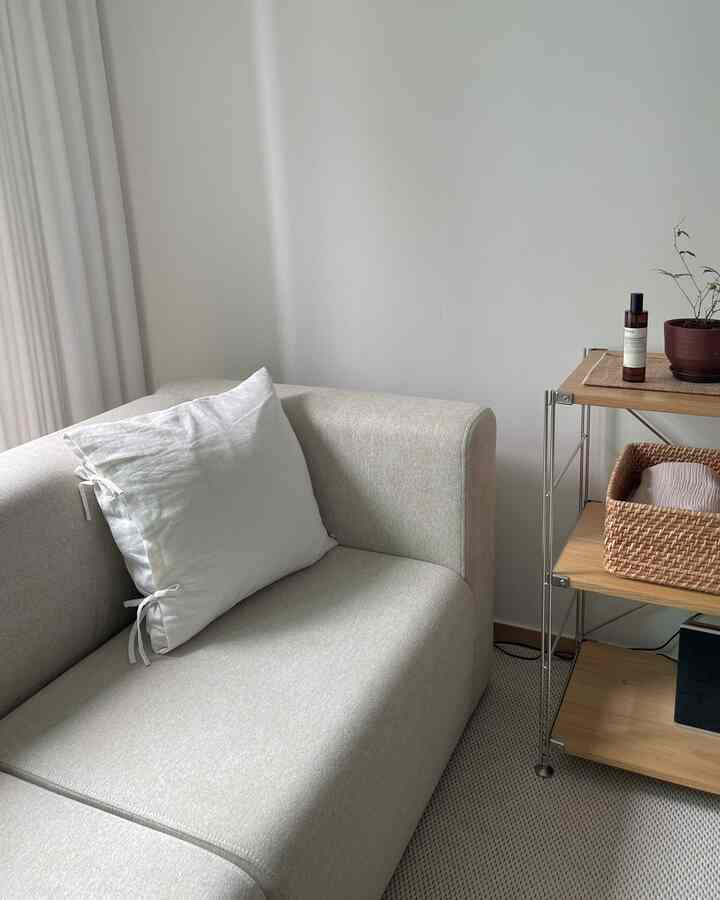 ナチュラルカラーのリビング、ベージュのソファと白いクッション、木製の棚とラタンバスケットが調和したシンプルな空間