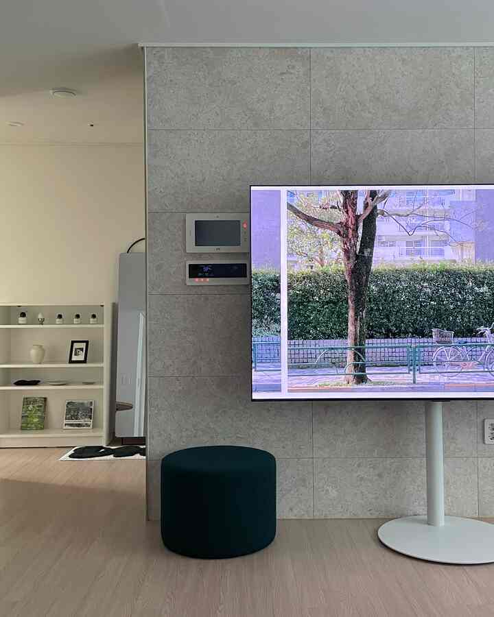 ナチュラルカラーとホワイトトーンのキッチンスペース、中央に黒いスツールと大型のOLEDテレビが配置されたモダンなインテリア