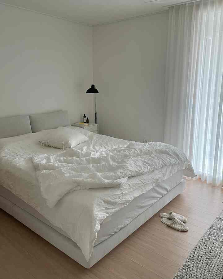 白いトーンの寝室、大きなベッドとシンプルなナイトテーブルが配置されたミニマルな空間