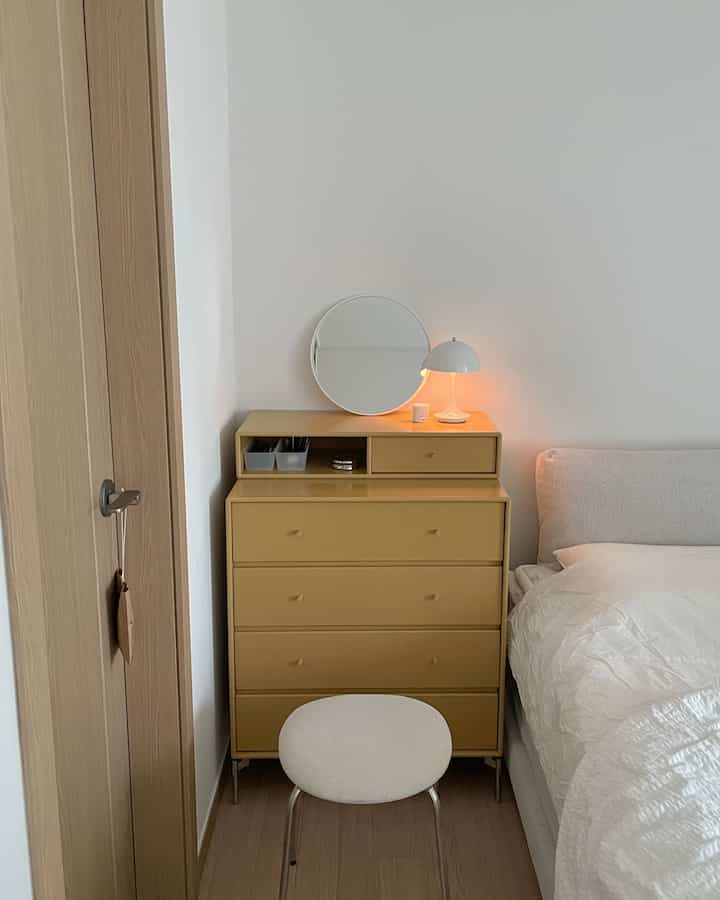 カーキ色のチェストと白いベッドが配置されたシンプルな寝室のインテリア