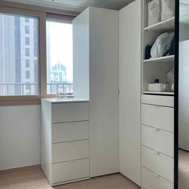 白とナチュラルカラーのコーナークローゼットとチェストが配置された、すっきりとして広く見える収納スペース