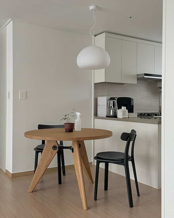 白と木目調が調和するモダンなダイニングルーム、丸いダイニングテーブルと黒い椅子が配置されたコンパクトなキッチン空間