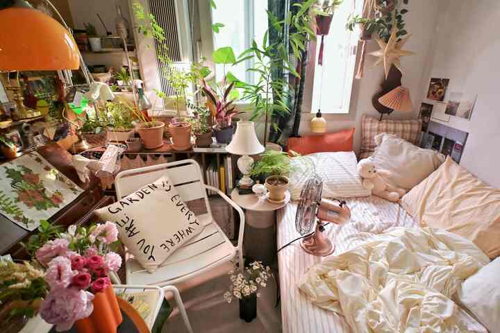 ナチュラルなトーンと植物が調和した2坪ほどの居心地の良い寝室、クッションと照明が配置されたマキシマリズムスタイルの空間