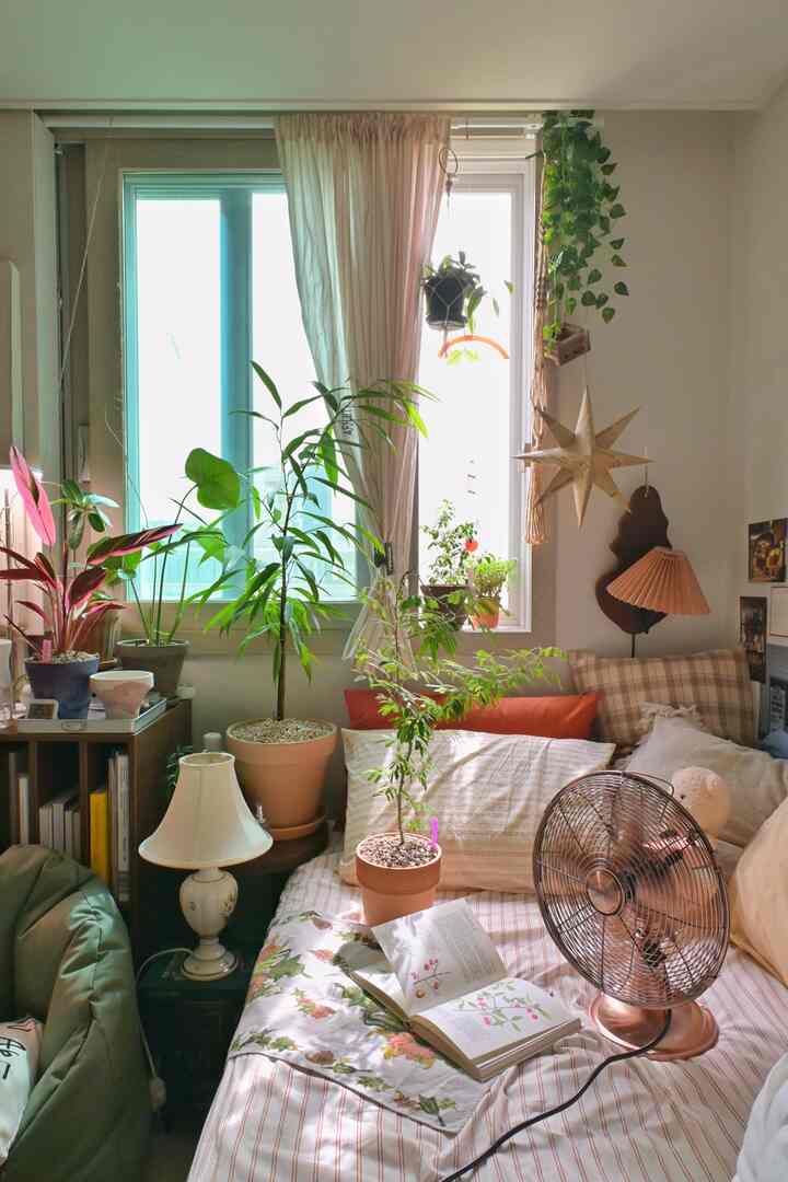 白を基調とした落ち着いた寝室に、多様な植物が窓辺とベッドに配置された、自然な雰囲気のインテリア