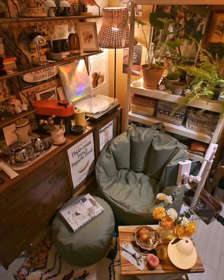 暖かいブラウンとグリーンのトーンのワンルーム、ビーンバッグ、LPターンテーブル、コーヒーマシンが配置された雰囲気あるホームカフェインテリア