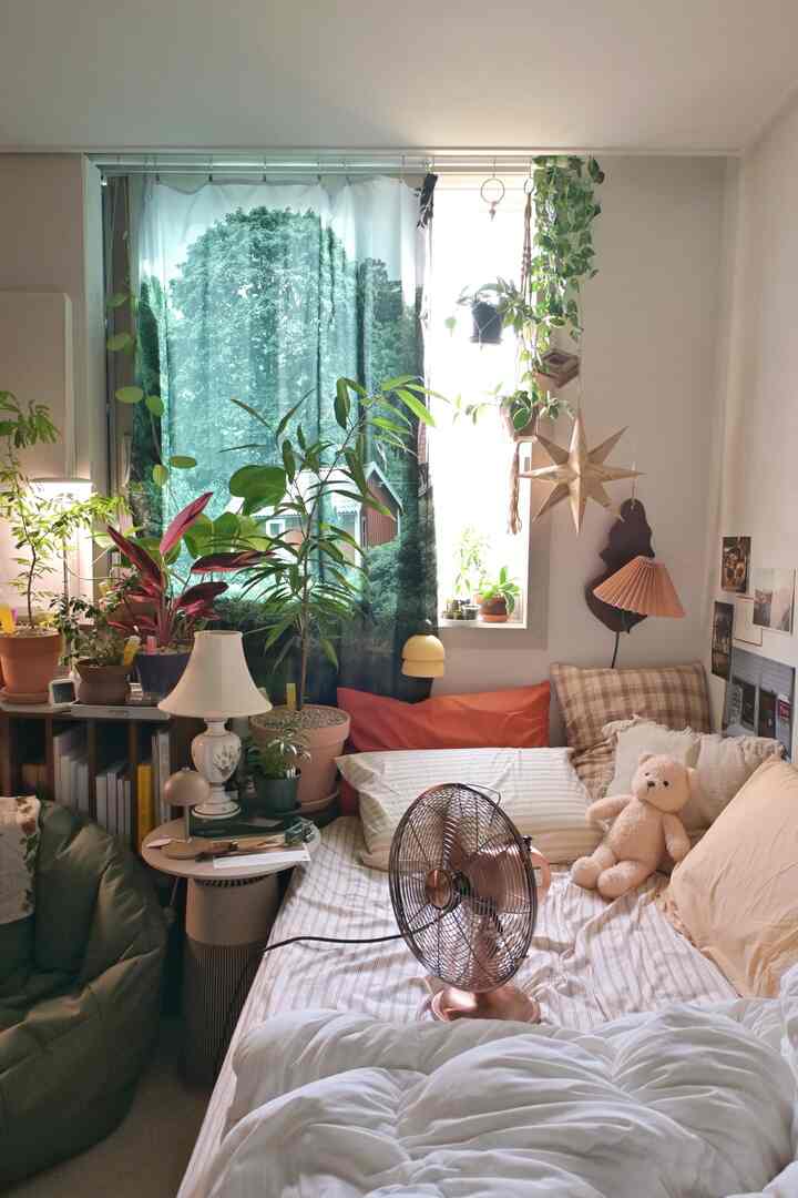 緑の植物と自然の風景のカーテンが印象的な、低いベッドフレームと多様な枕とクッションが配置された居心地の良い寝室