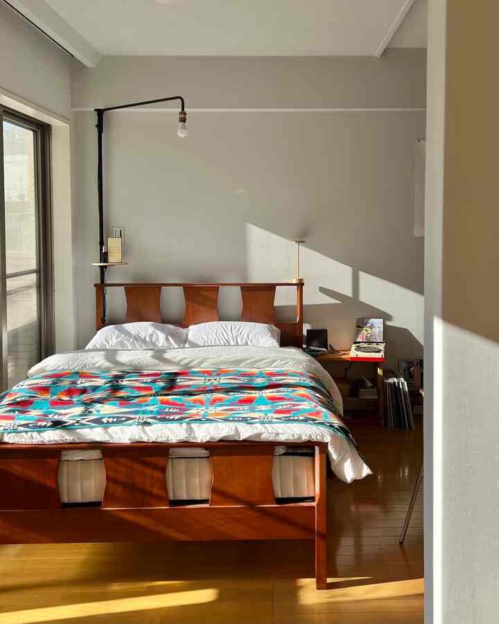 ナチュラルなトーンのブラウンのベッドフレームと白い寝具、カラフルなベッドカバーがある清潔感のある寝室