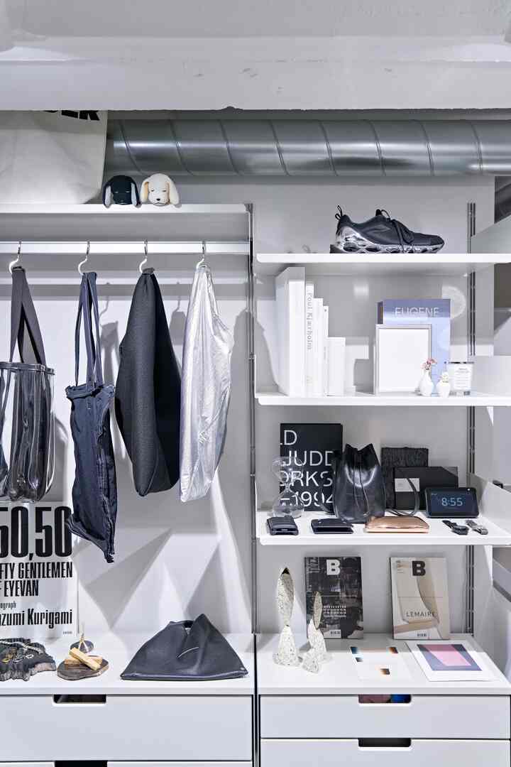 白を基調としたモダンでミニマルな空間、収納とディスプレイを兼ねた白い棚に鞄や本が整然と配置された雰囲気のあるインテリア