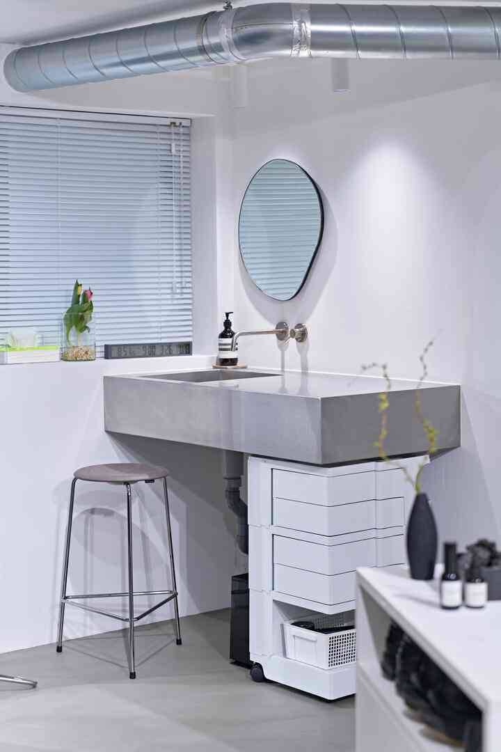 白とステンレスの素材が際立つミニマルなバスルーム、スツールと収納キャビネットが配置された実用的なインテリア