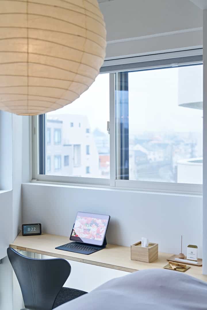 白と木目調の調和が取れた窓際のワークスペース、大きなペンダントライトとシンプルな小物が落ち着いた雰囲気を演出