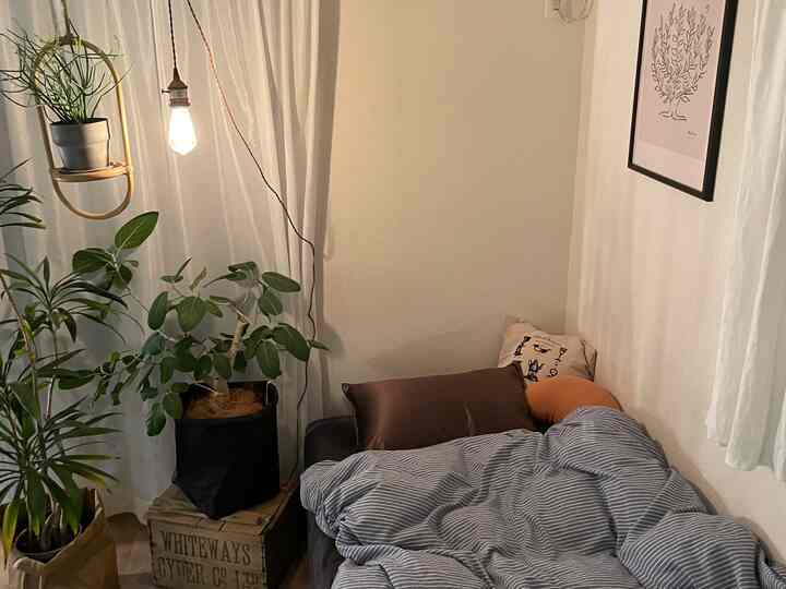 白い壁とカーテン、ベッドに茶色のクッション、ペンダントライトが配置された温かみのある一人暮らしの寝室