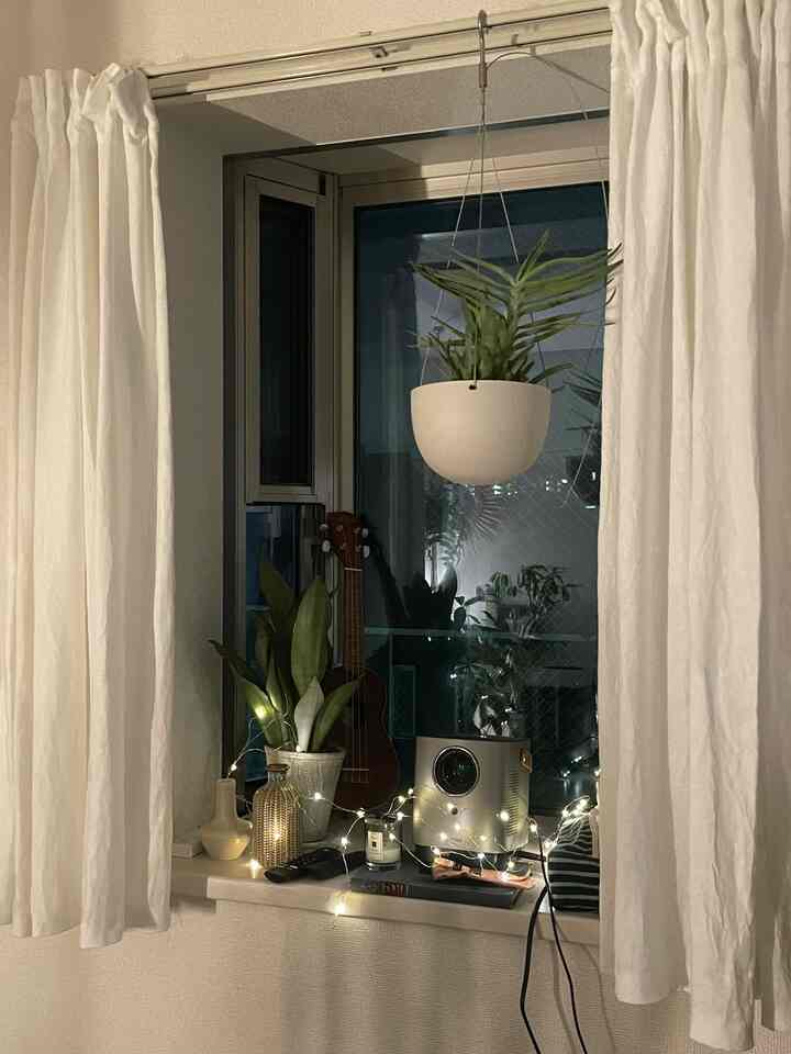 アイボリーのカーテンと植物、ストリングライトが配置された居心地の良いベランダの窓辺