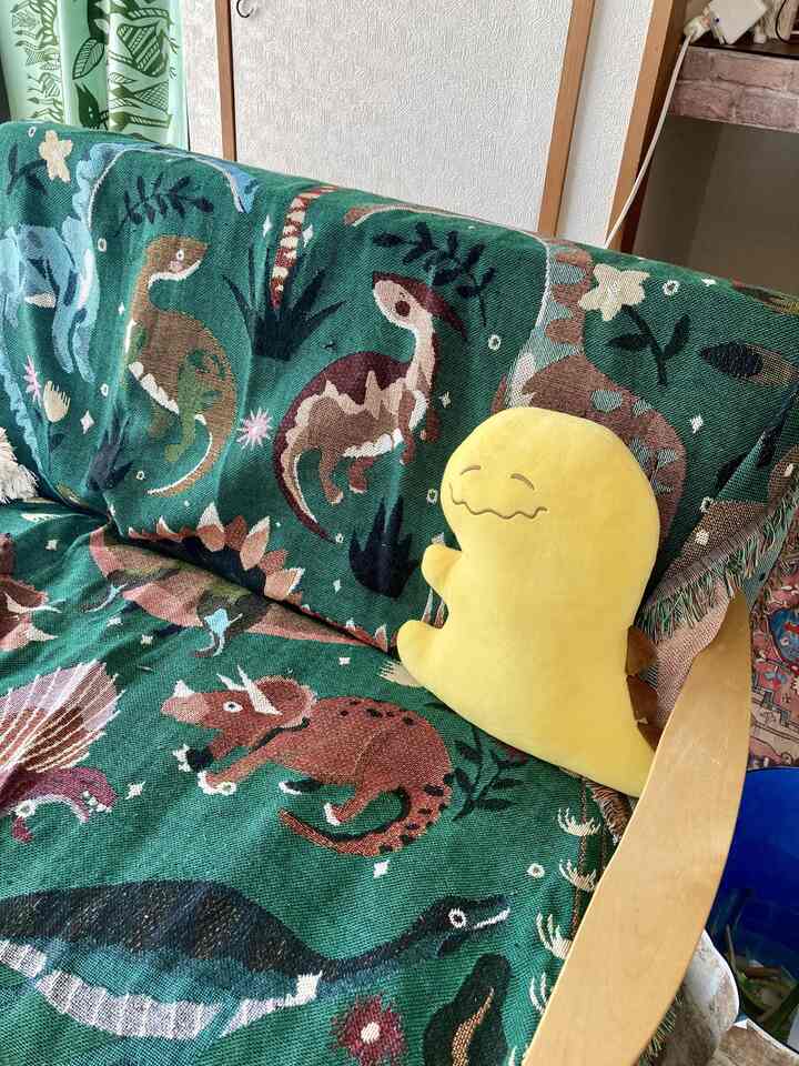 緑色の恐竜柄ブランケットと黄色の恐竜クッションが置かれたリビングのソファ