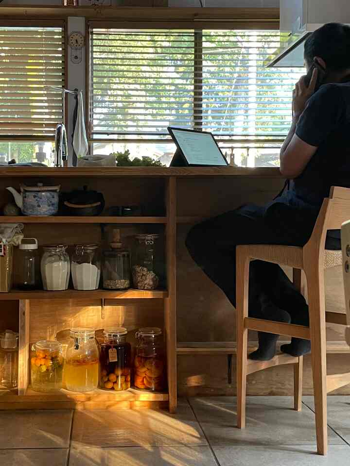 暖かい木調とベージュのタイルが調和したキッチン、カウンタースツールとオープン棚が配置されたホームオフィス空間